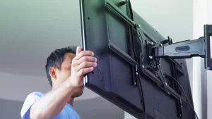 Técnico instalando televisão em suporte articulado na parede, ajustando a fixação do aparelho.