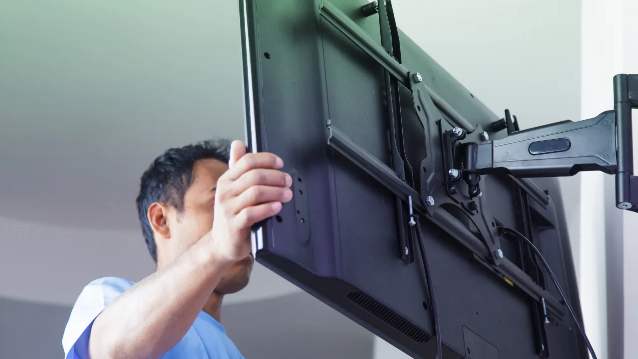 Técnico instalando televisão em suporte articulado na parede, ajustando a fixação do aparelho.